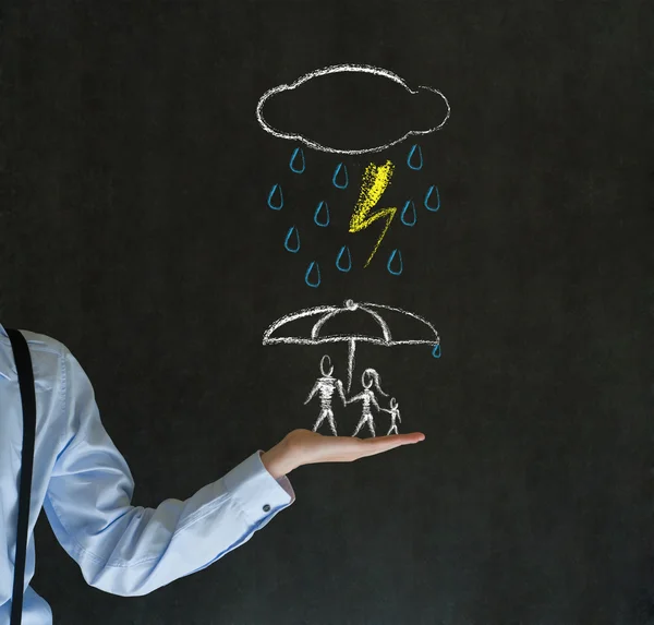 Insurance businessman holding out hand protecting family from natural disaster on blackboard background — Stock Photo, Image