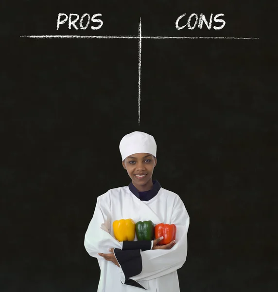 African american woman chef with chalk pros and cons on blackboard background — Stock Photo, Image