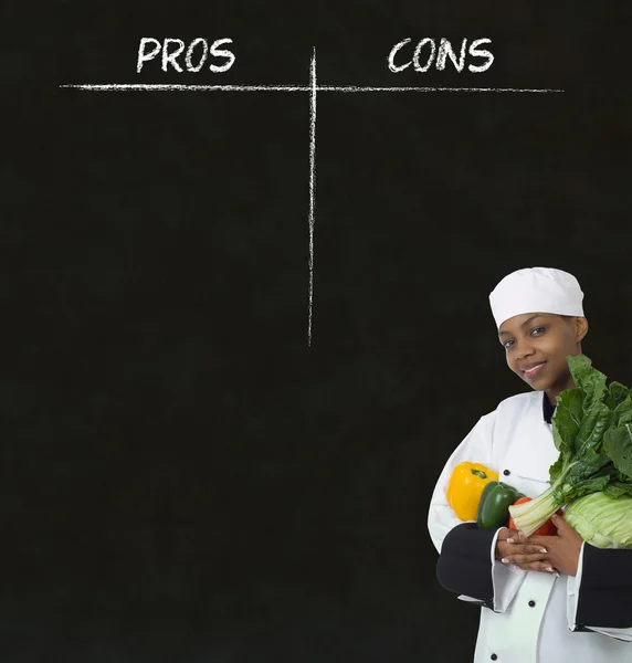 African american woman chef with chalk pros and cons on blackboard background — Stock Photo, Image