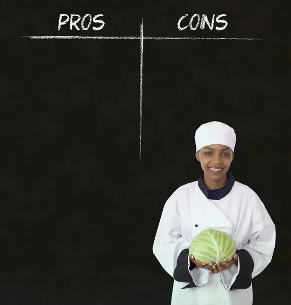 African american woman chef with chalk pros and cons on blackboard background — Stock Image African american woman chef with chalk pros and cons on blackboard background Stock Image