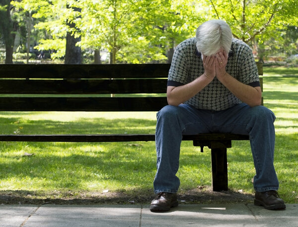 Депрессивный старик на скамейке запасных с фокусом на переднем плане
