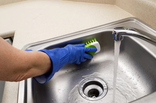 Женщина чистит раковину в голубых резиновых перчатках — стоковое фото