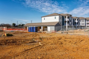 Horizontal shot of an apartment complext construction site with porta potties or portable toilets. clipart