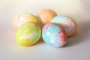Beyaz arkaplanda gölgesi olan renkli yumurtalar, yukarıdan gelen güneşin parlaklığıyla