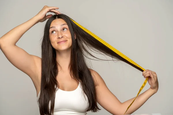 Молода Щаслива Жінка Показує Довжину Волосся Вимірювальною Стрічкою Сірому Фоні — стокове фото