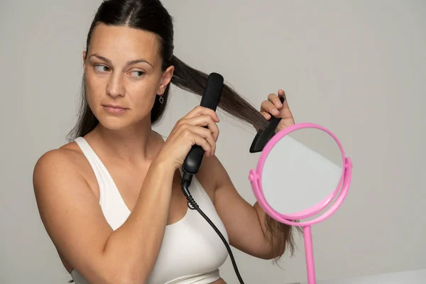 Giovane Bella Donna Raddrizzando Capelli Con Una Piastra Sfondo Grigio — Foto Stock