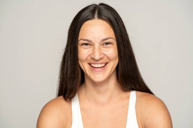 Makyajsız, uzun saçlı, gri arka planda mutlu bir kadın.