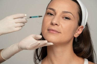 Gri arkaplandaki yüz doldurma işleminde tatmin olmuş genç bir kadının portresi