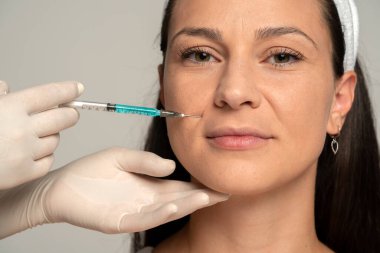 Gri arkaplandaki yüz doldurma işleminde tatmin olmuş genç bir kadının portresi