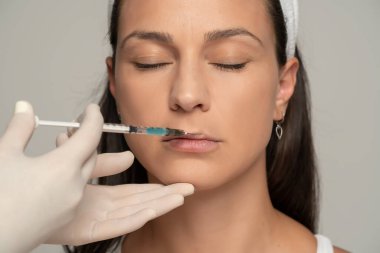 Gri arkaplandaki yüz doldurma işleminde tatmin olmuş genç bir kadının portresi