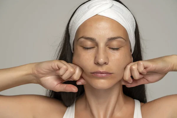 Uma Jovem Mulher Massageando Seu Rosto Fundo Cinza — Fotografia de Stock