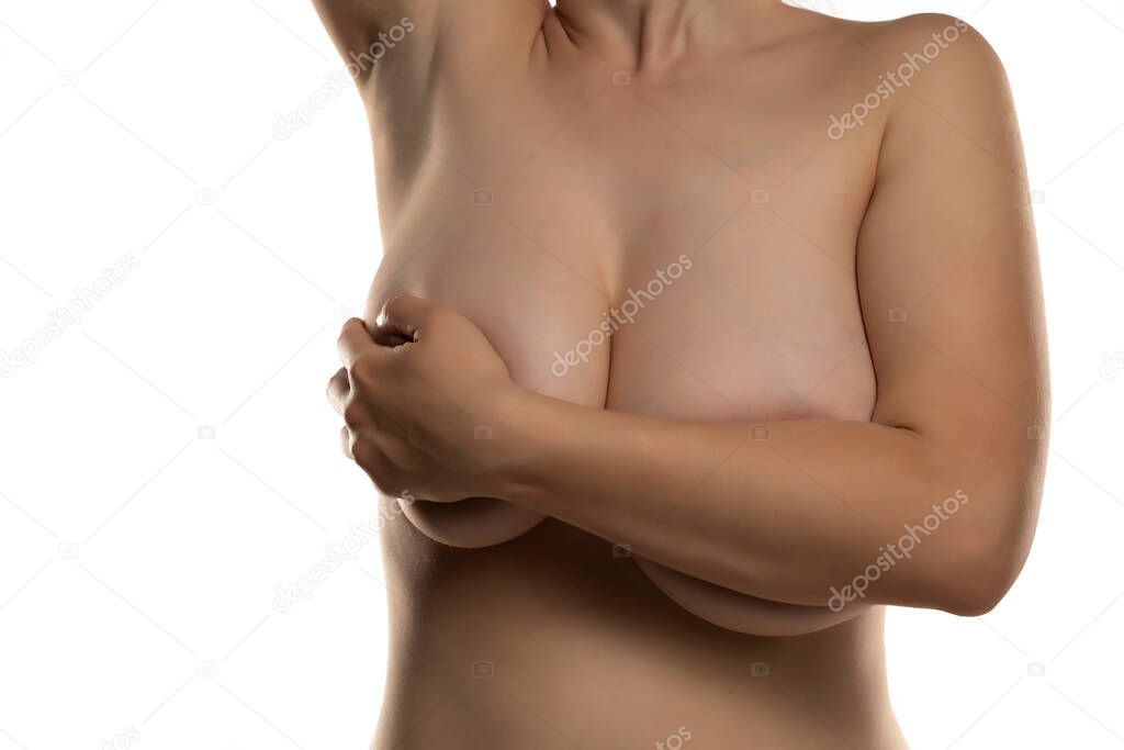the woman covers with one hand her large breasts on a white background