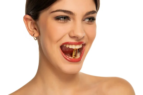 一个漂亮的年轻女子 她的牙齿上长着一颗白色背景的维生素丸 — 图库照片