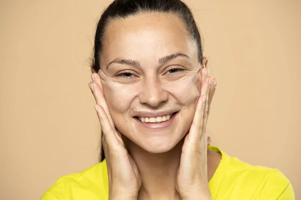 Detailní Záběr Mladé Ženy Aplikuje Maskér Její Obličej Béžové Pozadí — Stock fotografie
