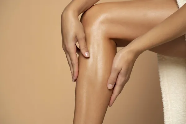 Close Een Vrouw Aanbrengen Crème Haar Benen Beige Achtergrond — Stockfoto