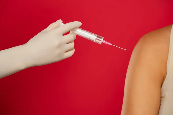 医生或护士在红色背景下向病人肩部注射Covid 19疫苗的特写镜头 — 图库照片
