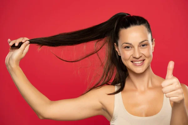 Genç Mutlu Bir Kadın Uzun Saçlarını Tutar Gösterir Kırmızı Arka — Stok fotoğraf