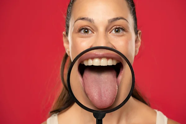 Молода Щаслива Жінка Показує Свій Здоровий Язик Через Збільшувальний Келих — стокове фото