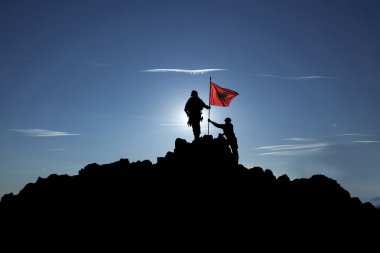Tanınmayan iki asker bir dağın tepesinde Arnavut bayrağını göndere çekiyor