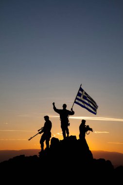Dağın tepesinde Yunan bayrağı taşıyan tanınmayan üç silahlı asker.