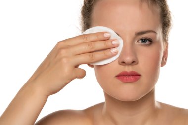 Beyaz arka plandaki makyajı silmek için pamuk pedi kullanan genç sarışın kadın.