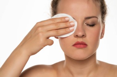 Sarışın güzel bir kadının portresi beyaz bir arka planda pamuk pedi ile yüzündeki makyajı temizliyor.