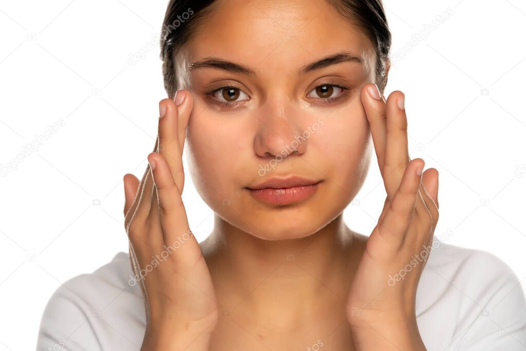 Head shot of a young beautiful woman applies concealer under her eyes on a white background
