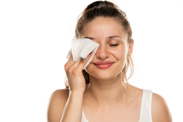 一个面带微笑的女人在白色的背景上用湿湿的湿巾擦去脸上的化妆品 — 图库照片