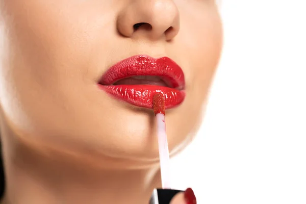 a woman applies red lip gloss to her lips on a white background