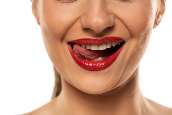 Young smiling woman with red lipstick touching her  her teeth with her tongue on a white background