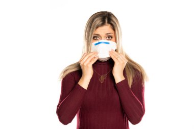 Beyaz bir arka planda yüzü maske takmış, mor elbiseli, üzgün bir sarışın.