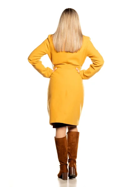リアビューのブロンドでA黄色のコートと革のブーツ上の白い背景 — ストック写真