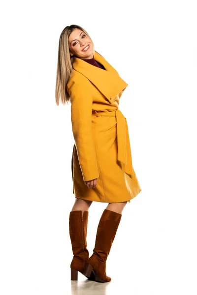 Junge Hübsche Lächelnde Blondine Gelbem Mantel Und Lederstiefeln Auf Weißem — Stockfoto