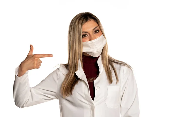 Młoda Piękność Kobieta Lekarz Wskazując Jej Twarz Medyczna Maska Białym — Zdjęcie stockowe