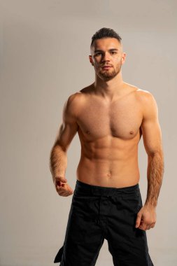 Siyah şortlu, gri arka planda poz veren MMA dövüşçüsü.