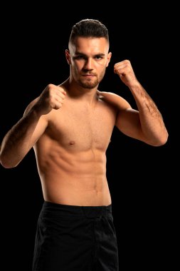 Siyah şortlu, siyah arka planda poz veren MMA dövüşçüsü.