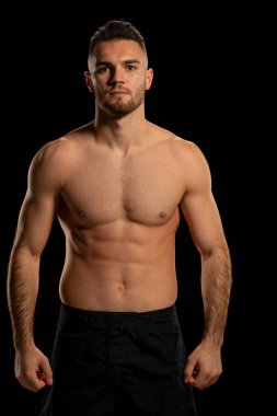 Siyah şortlu, siyah arka planda poz veren MMA dövüşçüsü.