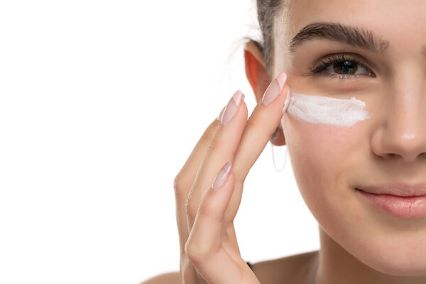 portrait of a young smiling teen girl applying cosmetic product under her eyes on a white background