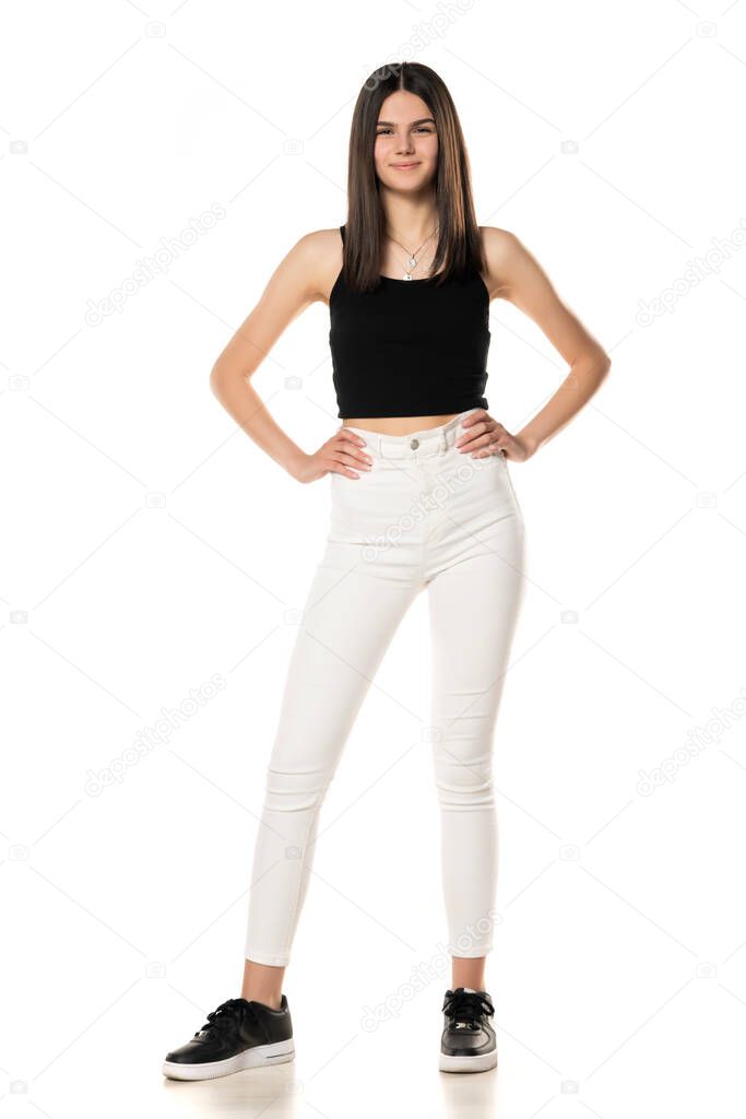 a teenage girl in white jeans and a black shirt stands on a white background