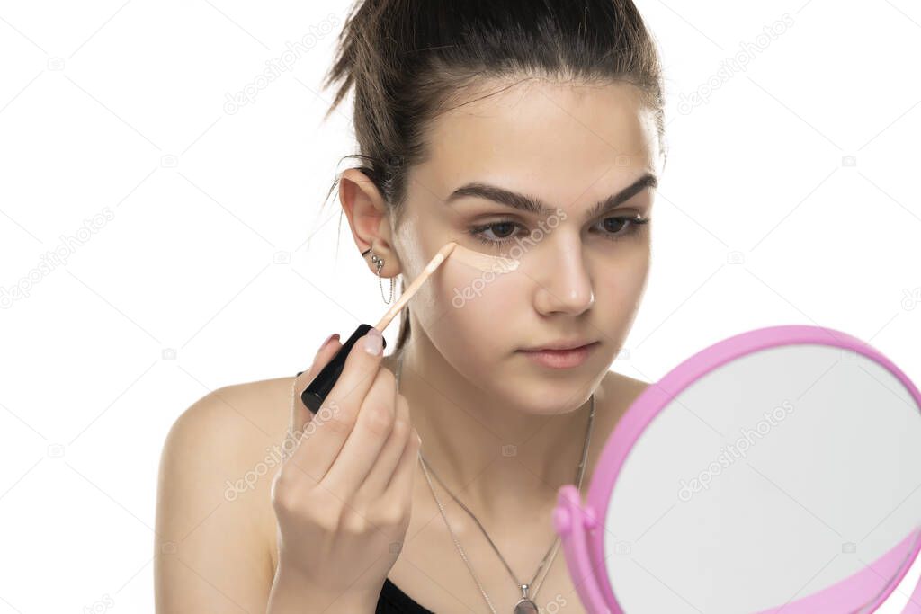 teen girl applyes concealer under her eyes on white background