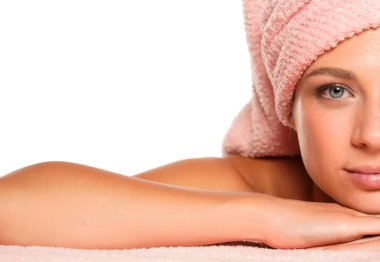 Mavi gözlü, beyaz bir arka planda kafasında havluyla poz veren güzel bir kadının yarım portresi.