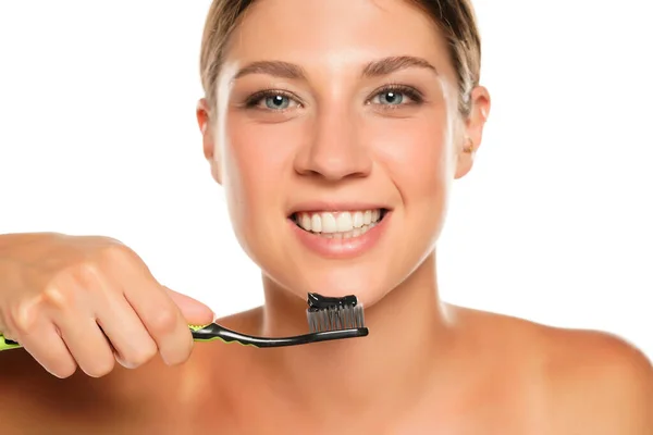 幸せな若い女性を保持歯ブラシ付き黒炭ペースト白の背景に — ストック写真