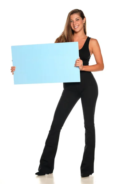 一个年轻的广告女郎穿着裤子和衬衫 在白色的背景上挂着一块空木板 — 图库照片