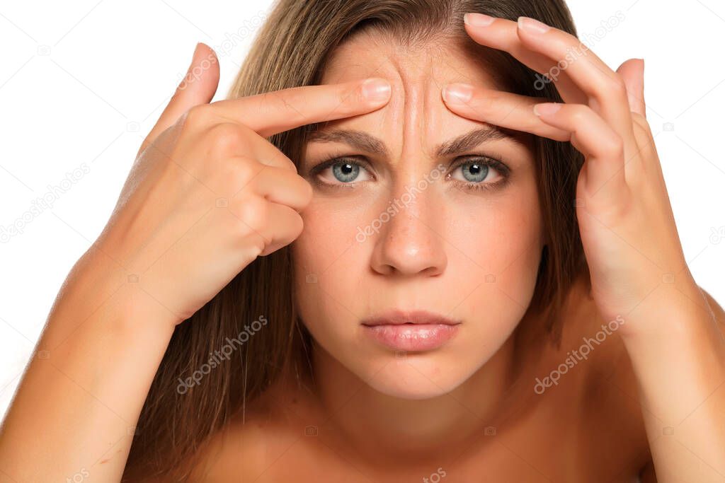 a young woman squeezes the wrinkles on her forehead on white background