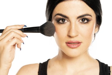 Makyaj fırçasıyla beyaz arka plana makyaj yapan güzel bir kadın.