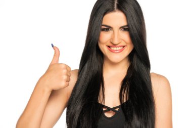 Uzun siyah saçlı ve makyajlı güzel bir genç kadın beyaz arka planda baş parmak gösteriyor.