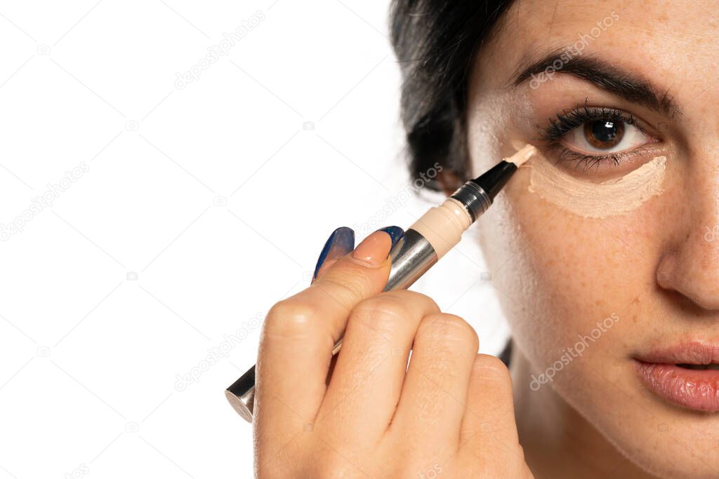 Half portrait of young beautiful woman applying concealer with applicator on white background