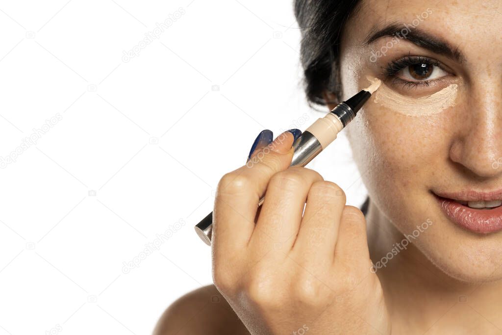 Closeup of young beautiful woman applying concealer with applicator on white background