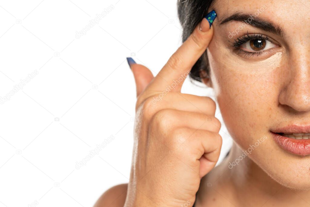 beautiful young freckled woman applying concealer with her finger on white background