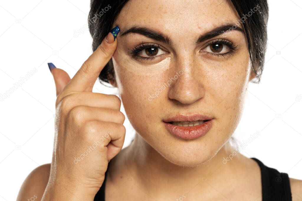 beautiful young freckled woman applying concealer with her finger on white background